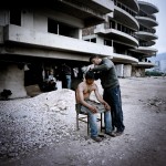 Greece, Patras. Mustafa cuts Arif's hair outside an abandoned building where they squat.