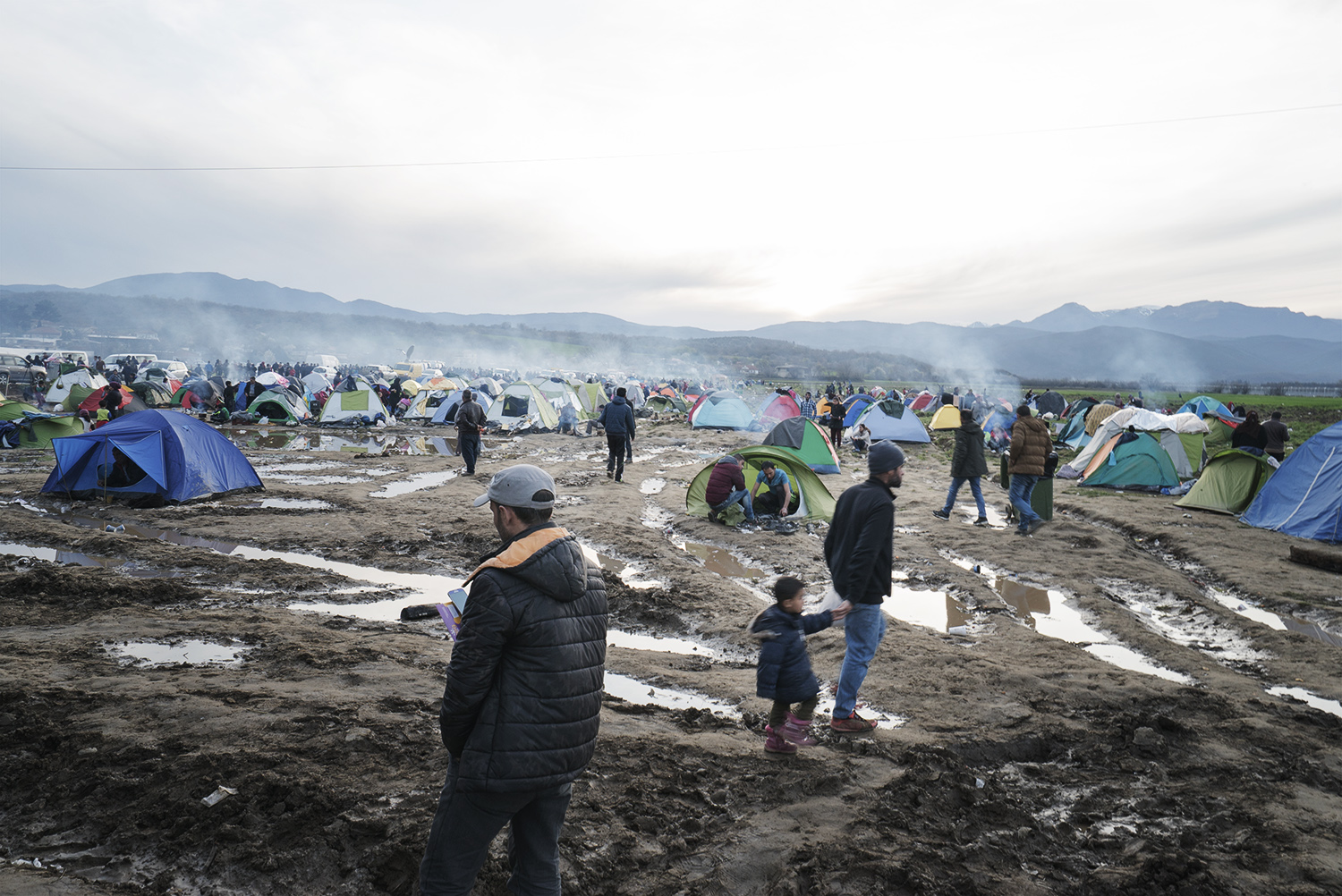 Greece, Idomeni border. Refugees walking down the muddy field, where camping tends have been set up in view of crossing the border. During the first week of March, 50 persons per day were allowed to cross the border with Macedona according to the date of arrival in Greece. As of the second week of March, border closed completely. No one was allowed to cross. As a result, that self-organized and not authorised refugee camp built arond Idomeni train -lane expaned dramatically. Greece, Idomeni border. The border between Greece and Macedonia has become a not recognized refugee camp where approx. 12.000 Syrian and iraqui refugees are awaiting for its reopening in the hope of achieving the German dream. As the meeting between EU and Turkey didn't lead to any changes on the ground, Syrian, Iraqui, Palestinians, Afghans, Pakistani refugees got trapped in that slot of the Greek territory with no way forward. No space for accommodating them is currently available in the existing camps (Diavata, Cherso and Nea Kavala) set up by the Greek Army. As such, prevented from crossing the border and not allowed to enter the camps, refugees will be relying on the international humanitarian assistance and ... on their hope, if it will be still there despite the life-threatening conditions in Idomeni. On March 18th, the EU and Turkey signed a new plan, according to which migrants arriving in Greece will be sent back to Turkey if they do not apply for asylum or their claim is rejected.