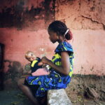 A woman holding a baby while talking with her friends.