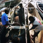 Fishermen check their equipment and talk in their pirogues beached at low tide in the early morning.