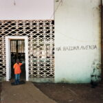 A boy stands at the entrance of a bar on the town's main road. (The graffiti on the wall reads: 'We sell Bazooka')